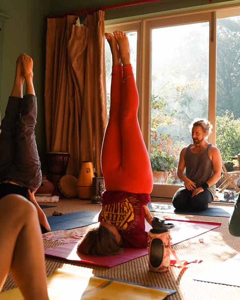 Yoga class with participants practicing headstands in a room with large windows.